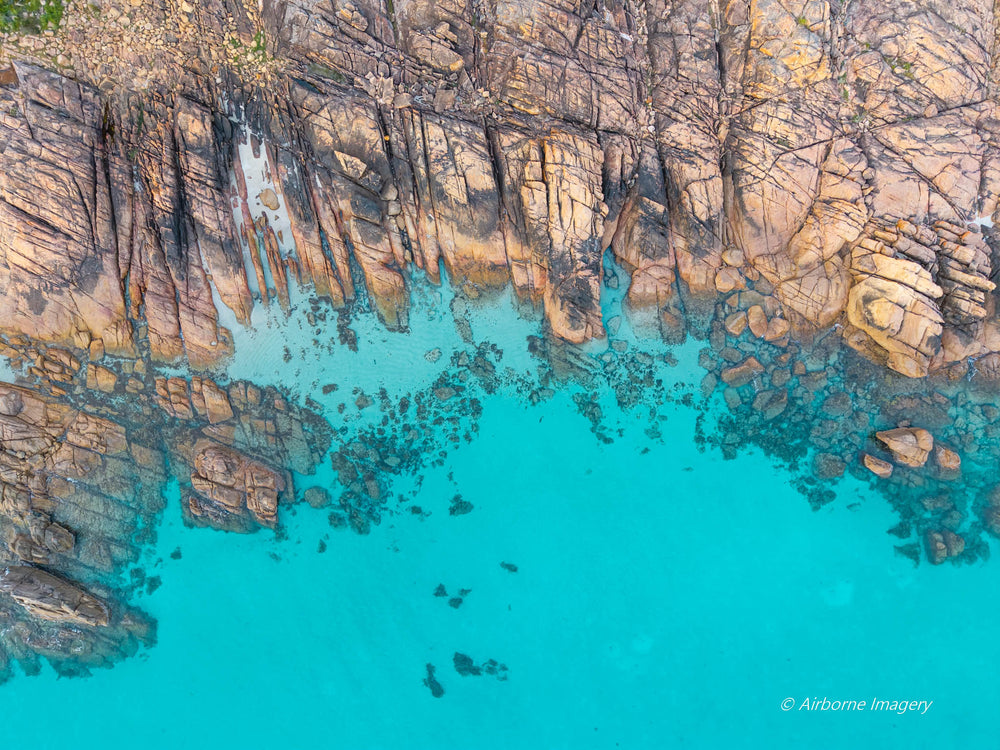 Overhead aerial view of Meelup Beach’s rocky coastline, with weathered granite ledges bordering vivid turquoise water and submerged boulders visible below.