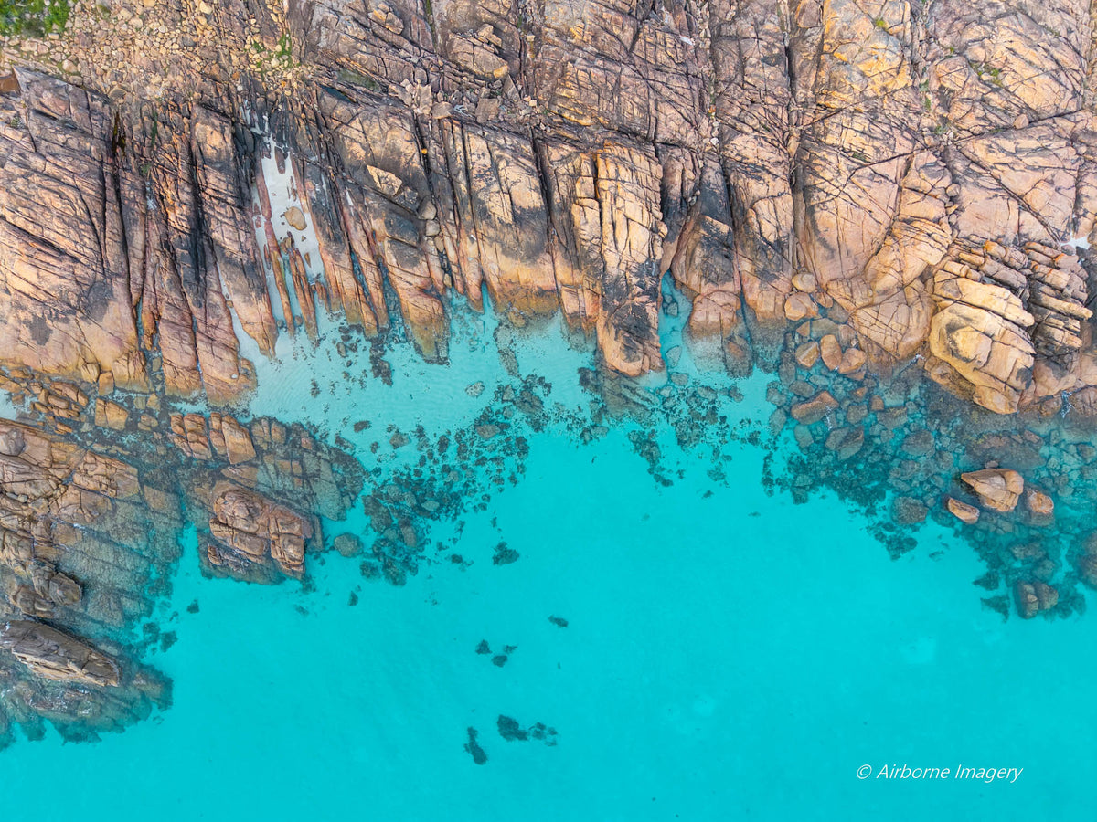 Overhead aerial view of Meelup Beach’s rocky coastline, with weathered granite ledges bordering vivid turquoise water and submerged boulders visible below.