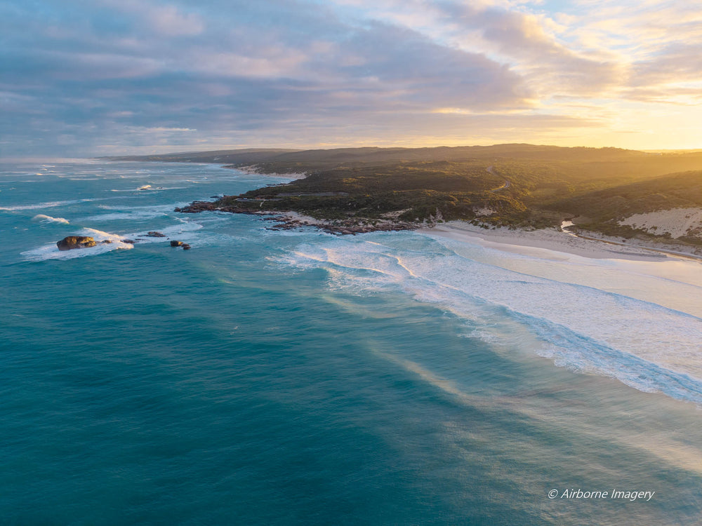 Aerial view of Redgate Beach, Margaret River at sunrise, with golden morning light, turquoise ocean, rolling waves and rugged South West WA coastline.