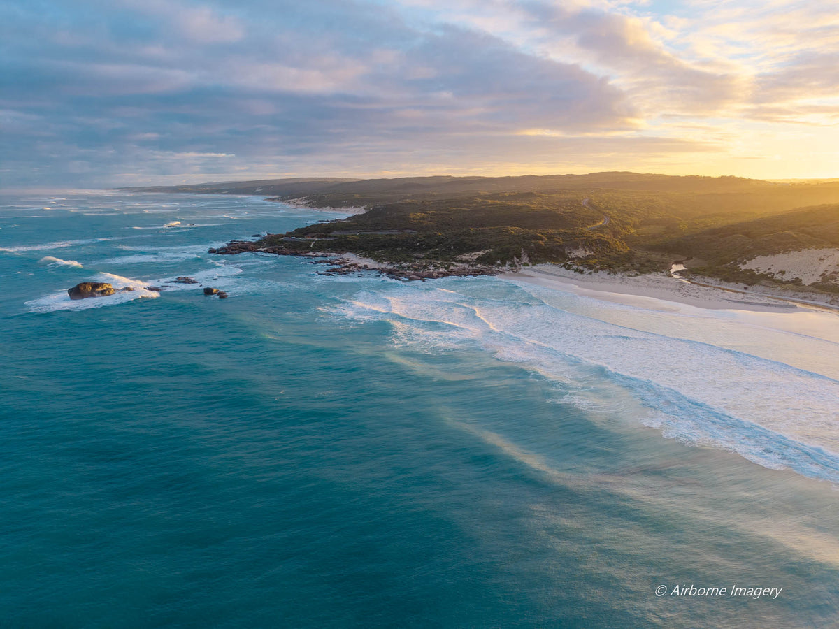 Aerial view of Redgate Beach, Margaret River at sunrise, with golden morning light, turquoise ocean, rolling waves and rugged South West WA coastline.