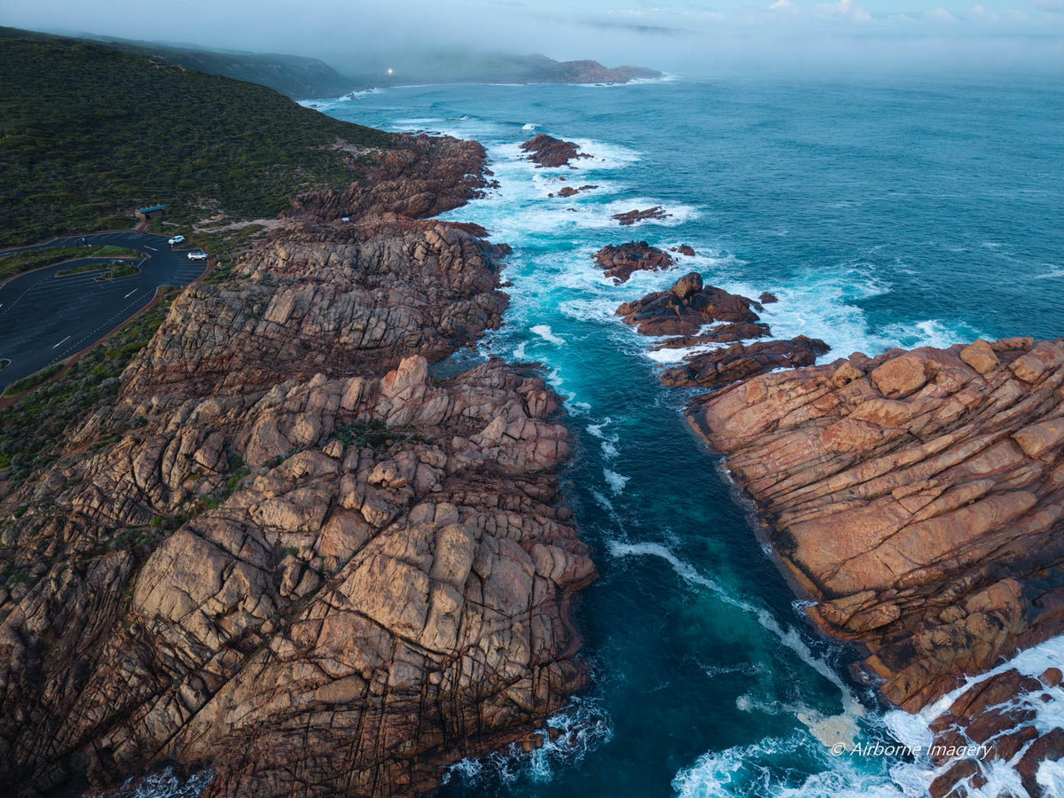 Aerial view of Canal Rocks in Yallingup, with rugged granite formations, deep blue ocean channels and white surf along a misty coastline.