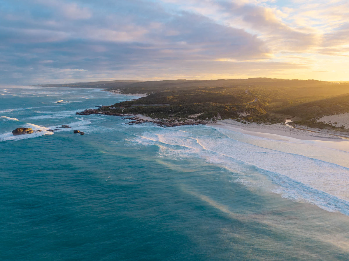 Aerial view of Redgate Beach, Margaret River at sunrise, with golden morning light, turquoise ocean, rolling waves and rugged South West WA coastline.