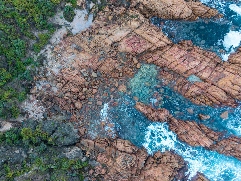 Overhead aerial view of the coastline at Sugarloaf Rock, with pink granite formations, clear turquoise rock pools, white surf and green coastal vegetation.