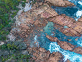 Overhead aerial view of the coastline at Sugarloaf Rock, with pink granite formations, clear turquoise rock pools, white surf and green coastal vegetation.