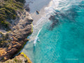 Aerial view of Redgate Beach near Margaret River, with turquoise water, white waves, a pale sandy cove and rugged rock ledges fringed by coastal greenery.